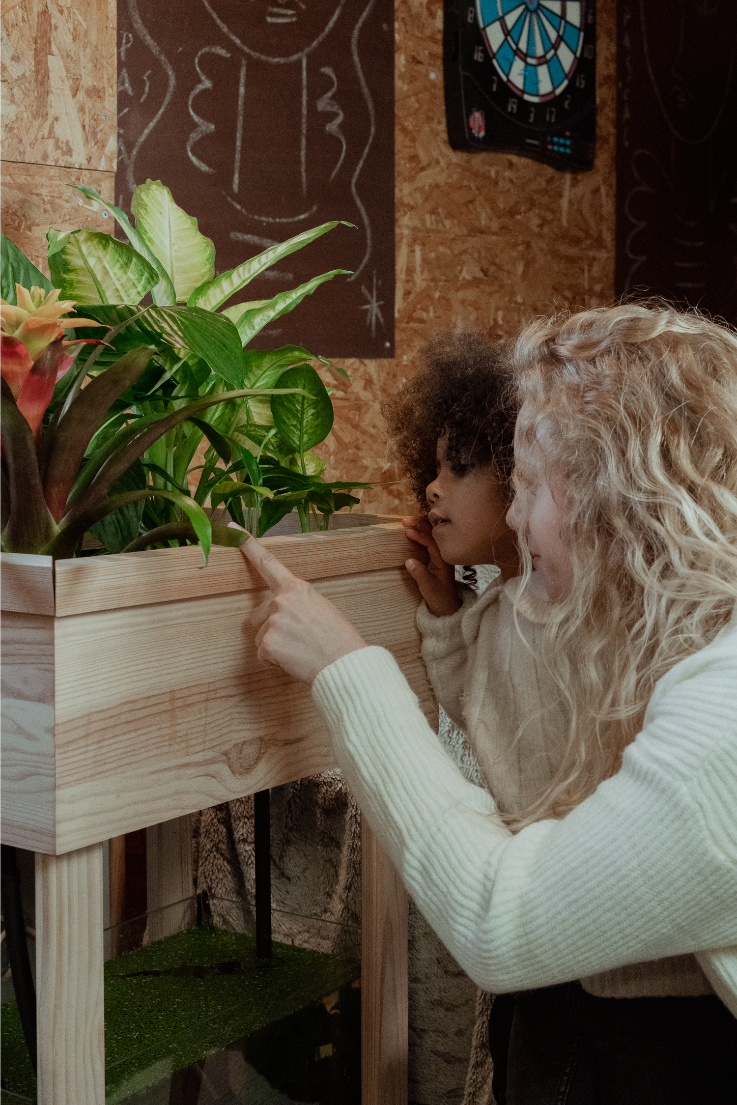 Une mère et sa fille sont dans un salon et observent de jolies plantes vertes qui sont situés dans le bac de culture de l'Aquapouss'Mini. On voit l'aquarium qui se situe en dessous du bac de culture avec des petits poissons orange.